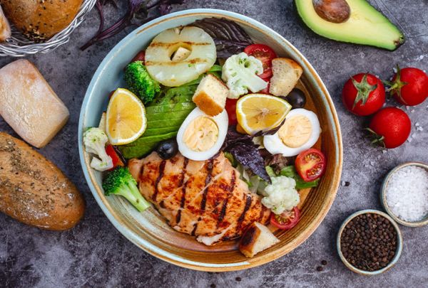 Draufsicht auf gesunden Diätsalat mit gegrilltem Hähnchen, Brokkoli, Blumenkohl, Tomaten, Avocado und Salat