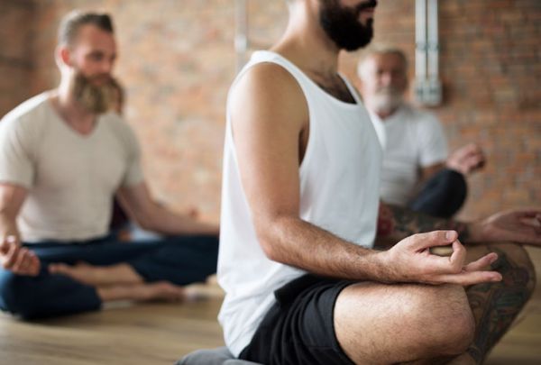 mehrere Männer sitzen im Lotussitz auf dem Boden und praktizieren Yoga
